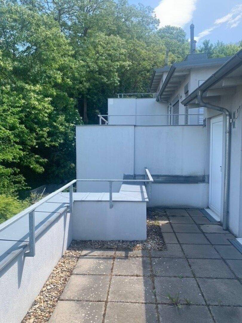Geräumige Außenterrasse mit Fliesenboden und Metallgeländer, umgeben von viel Grün.