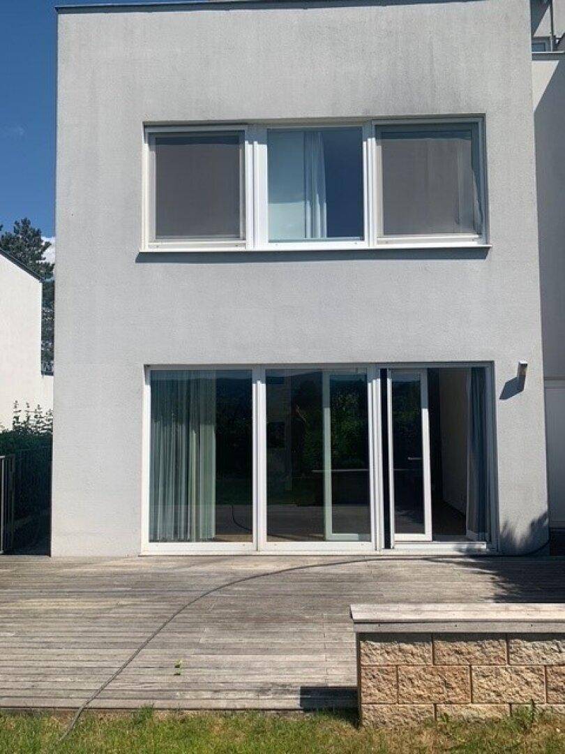 Moderne Gebäudefassade mit großen Glasfronten und einer Holzterrasse im Erdgeschoss.