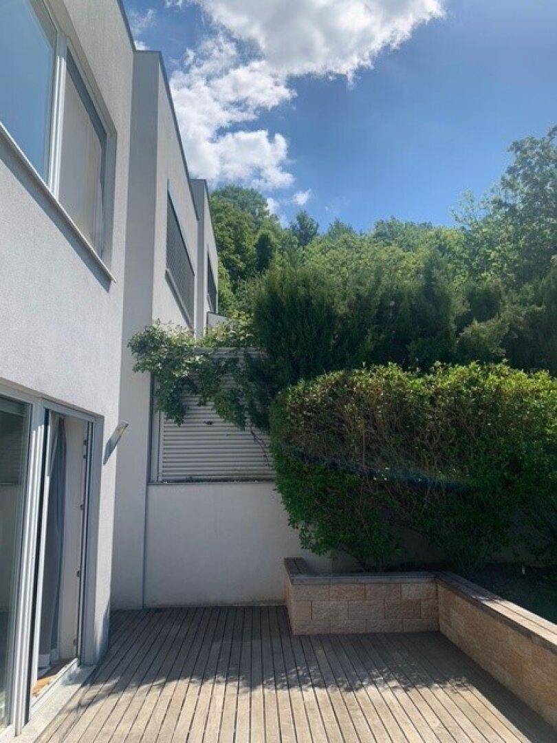 Seitliche Ansicht des Gebäudes mit Holzterrasse und einer bepflanzten Steinmauer.