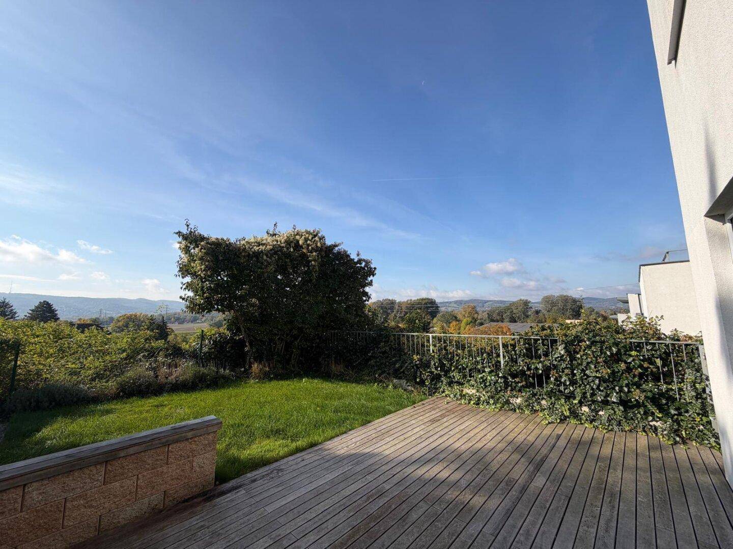 Geräumige Holzterrasse mit Blick auf die weite grüne Landschaft unter einem klaren Himmel.