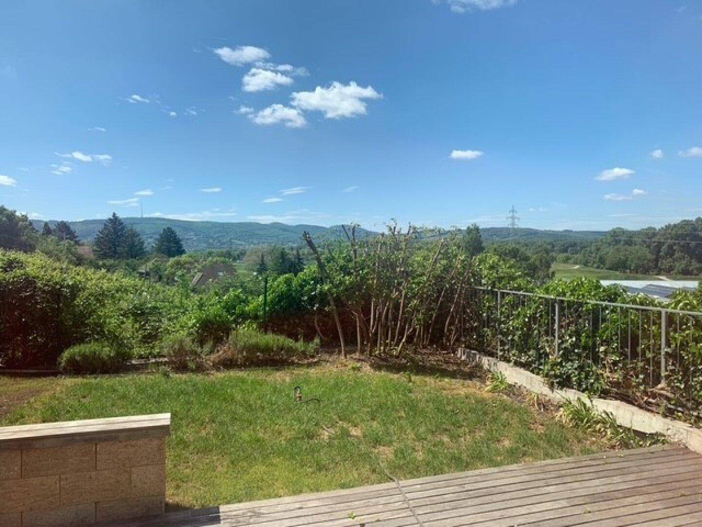 Großer Gartenbereich mit Rasenfläche und Holzterrasse, bietet einen weiten Blick ins Grüne.