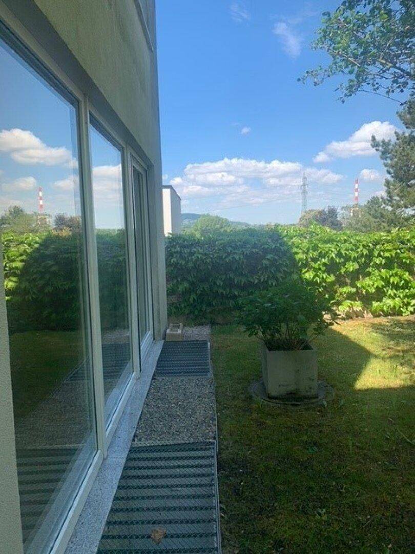 Gartenansicht mit großen Fenstern und üppiger Hecke, bietet einen weiten Blick in die Umgebung.
