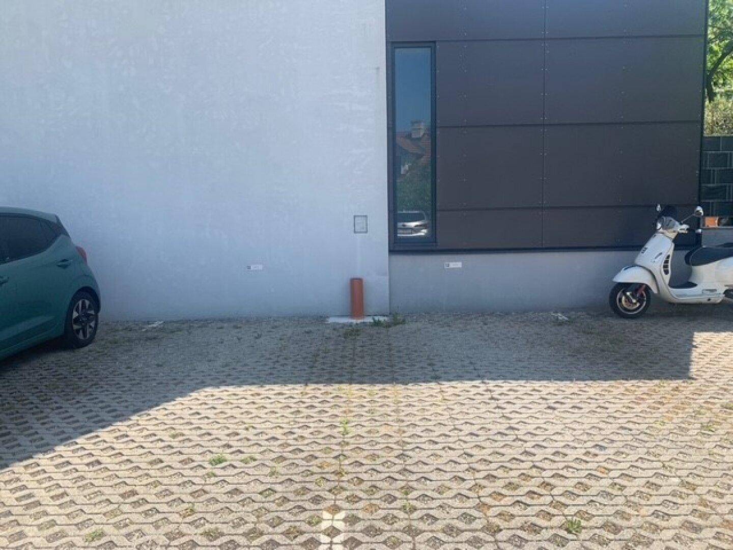 Außenparkplatz mit Rasengittersteinen vor einer modernen Gebäudefassade, bietet Stellflächen.