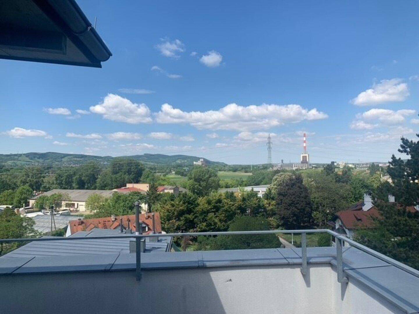 Weitläufiger Ausblick von einem Balkon auf eine Mischung aus Natur und städtischer Bebauung.
