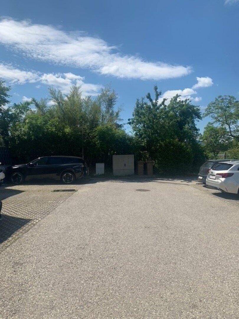 Großer Außenparkplatz mit mehreren Fahrzeugen, umgeben von Bäumen und Büschen im Hintergrund.