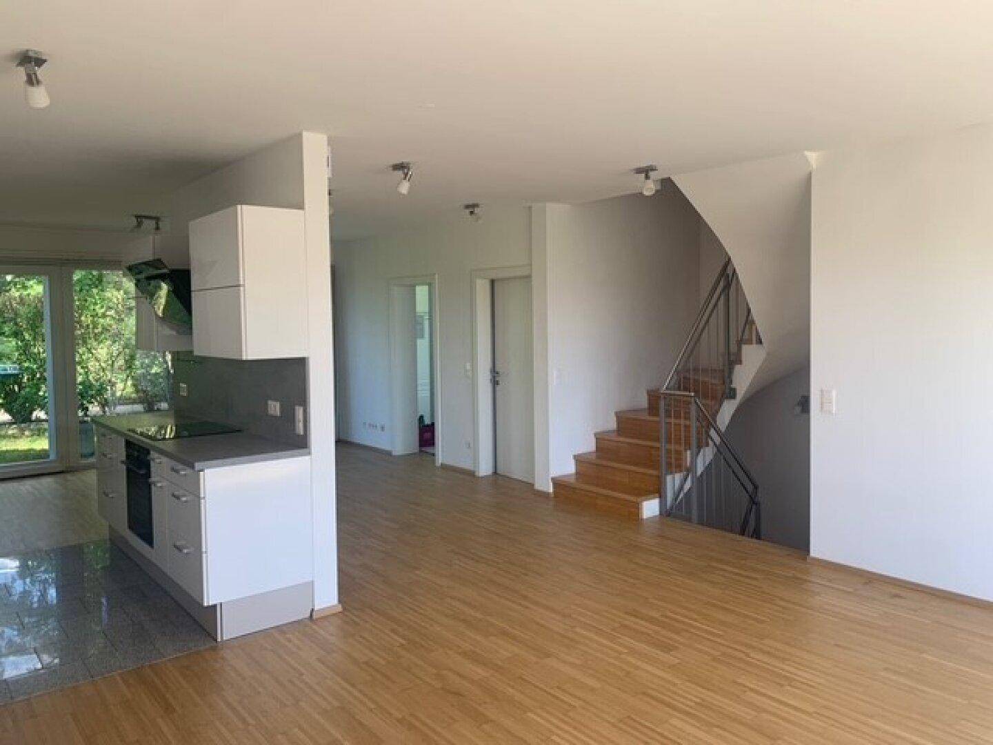 Moderne Küchenzeile mit weißen Schränken und angrenzender Holztreppe in einem offenen Wohnbereich.