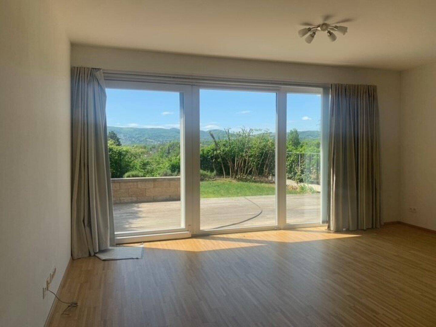 Helles Wohnzimmer mit großen Schiebetüren, Holzboden und Zugang zur Terrasse mit Gartenblick.