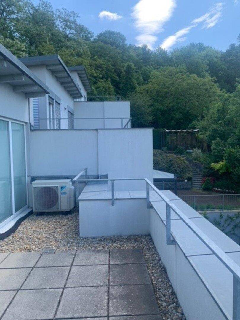Außenbereich mit Terrasse, Klimaanlage und Blick auf die bewaldete Umgebung.