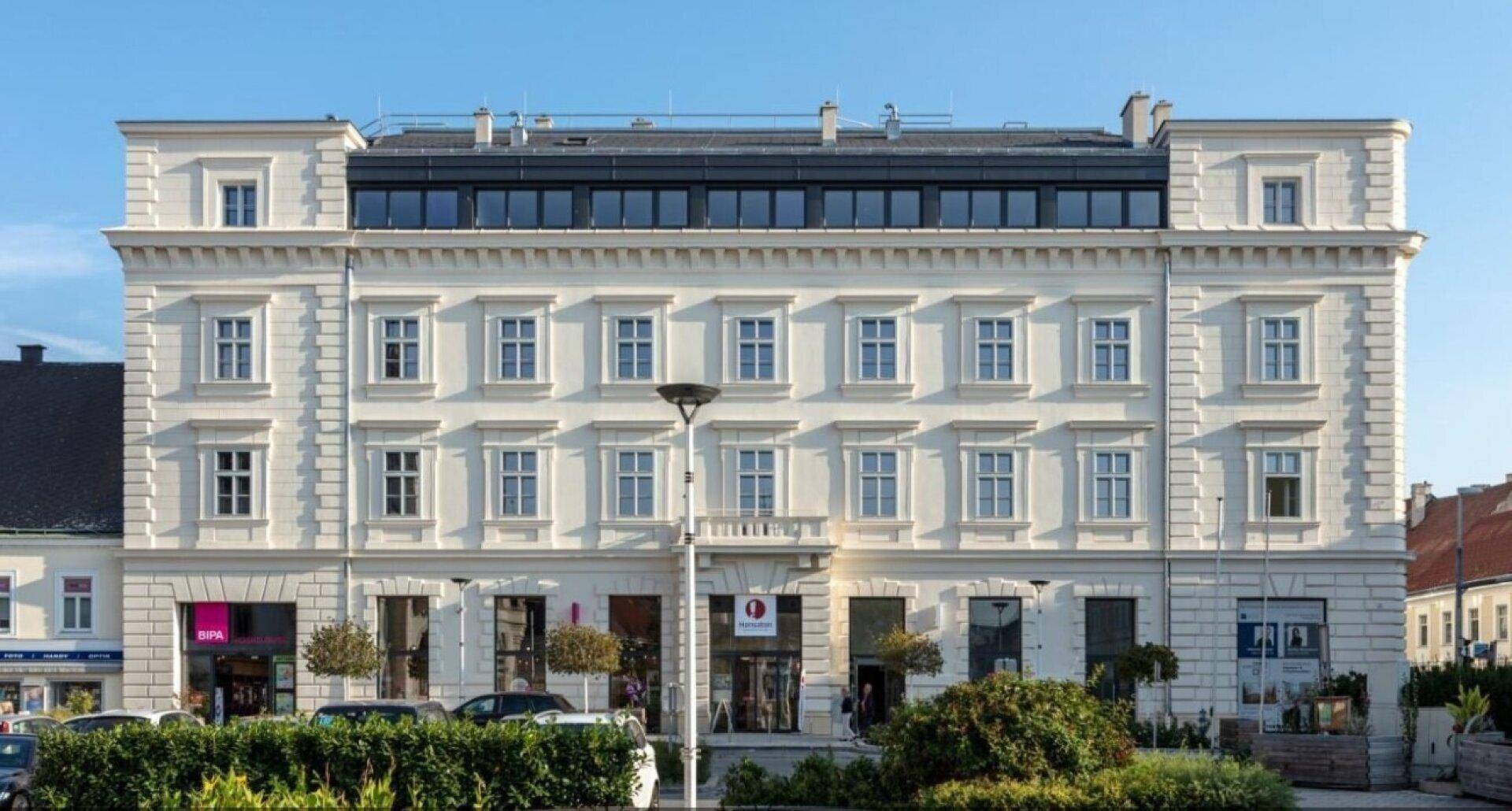 Historisches Gebäude mit klassischer Fassade und modernem Dachausbau in einer städtischen Umgebung.
