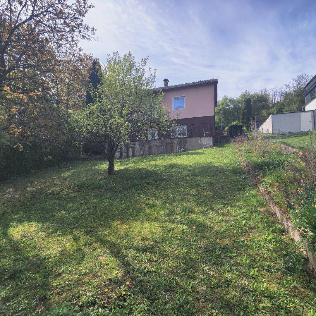 Rückansicht eines Hauses mit großem, leicht abfallendem Garten und umgebenden Bäumen.