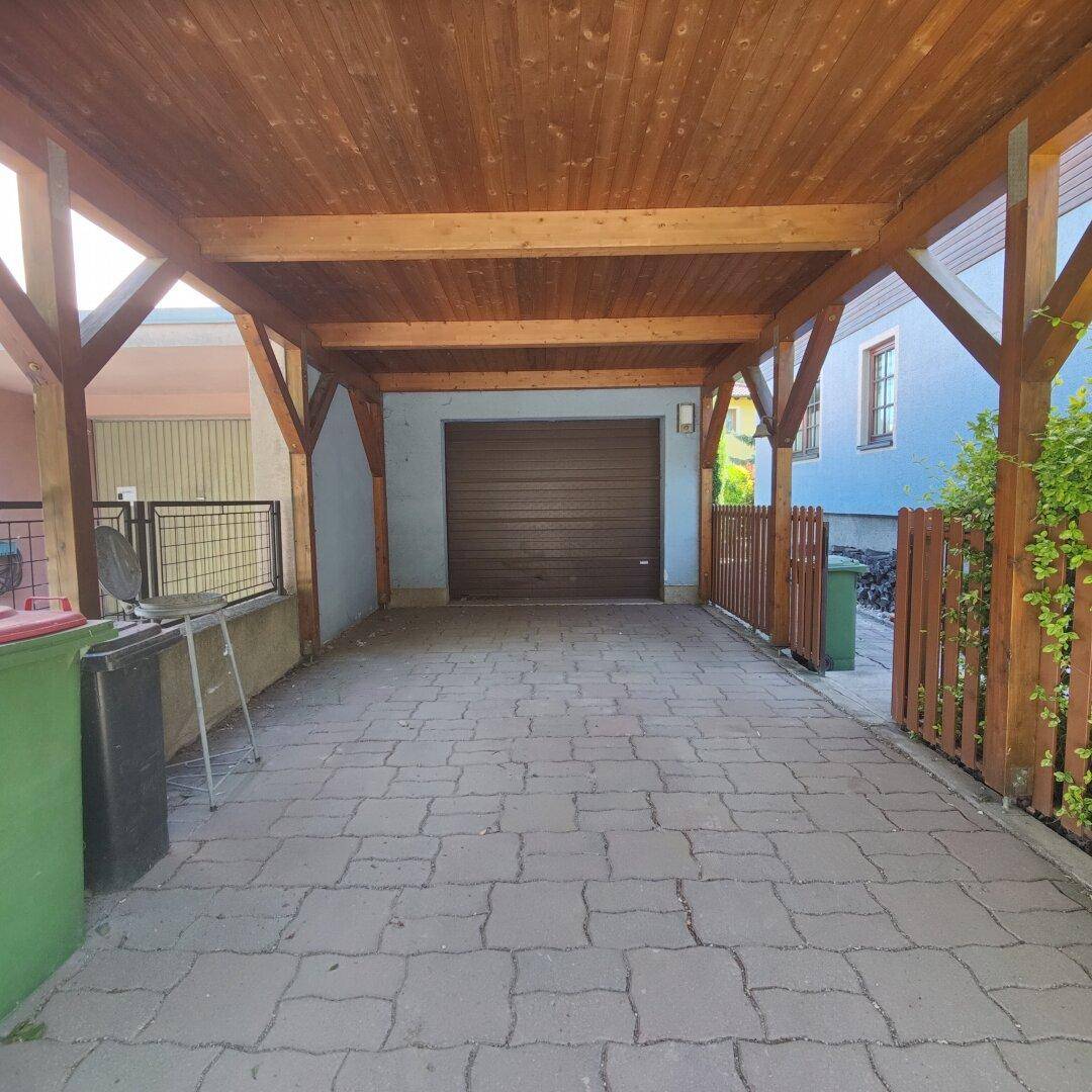 Überdachter Carport mit gepflasterter Einfahrt und Garagentor im Hintergrund.