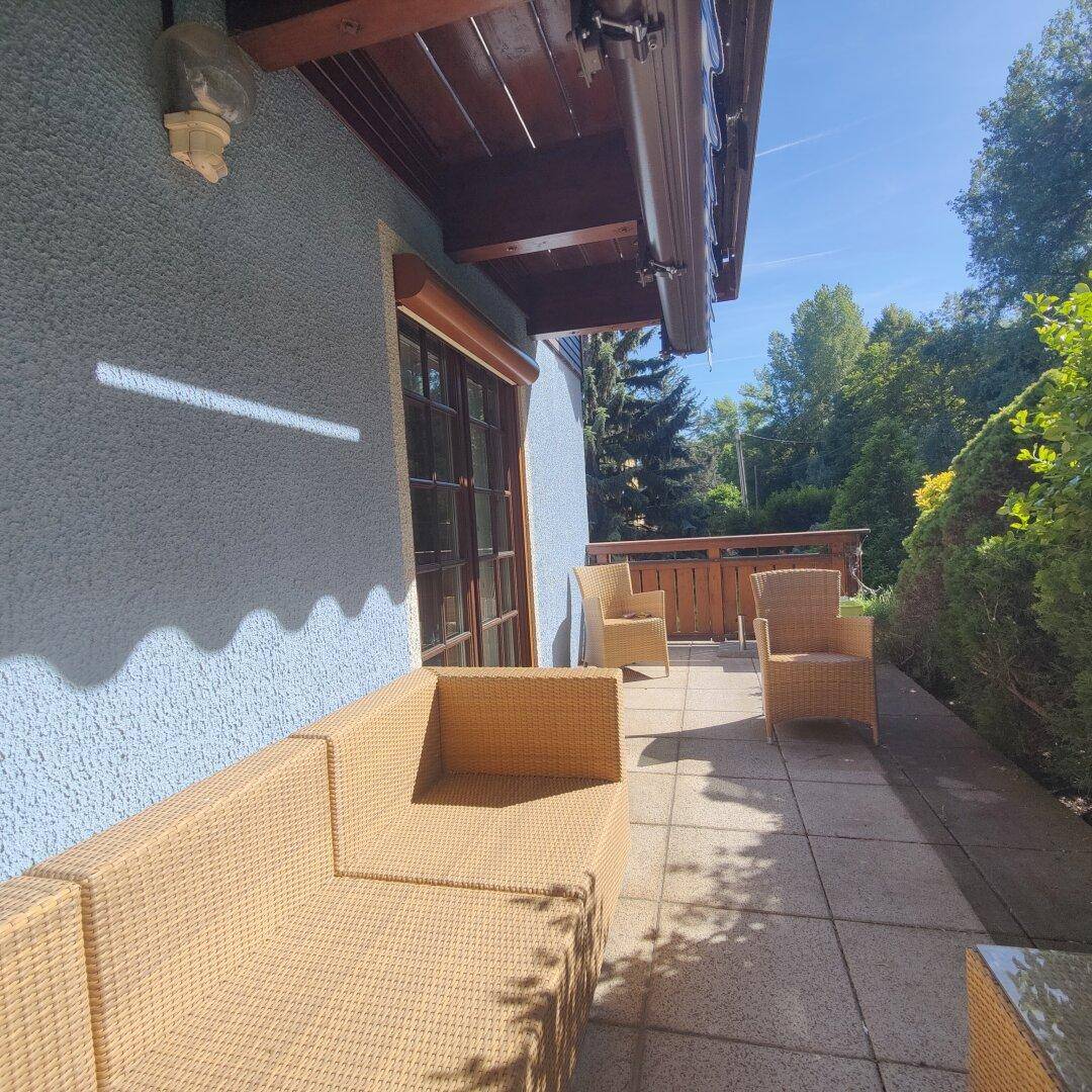 Geräumige Terrasse am Haus mit Korbmöbeln und Blick ins Grüne an einem sonnigen Tag.