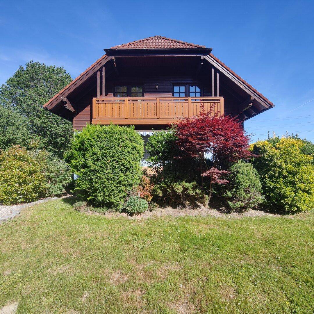 Charmantes Holzhaus mit traditionellem Balkon und üppiger Bepflanzung im Vorgarten.
