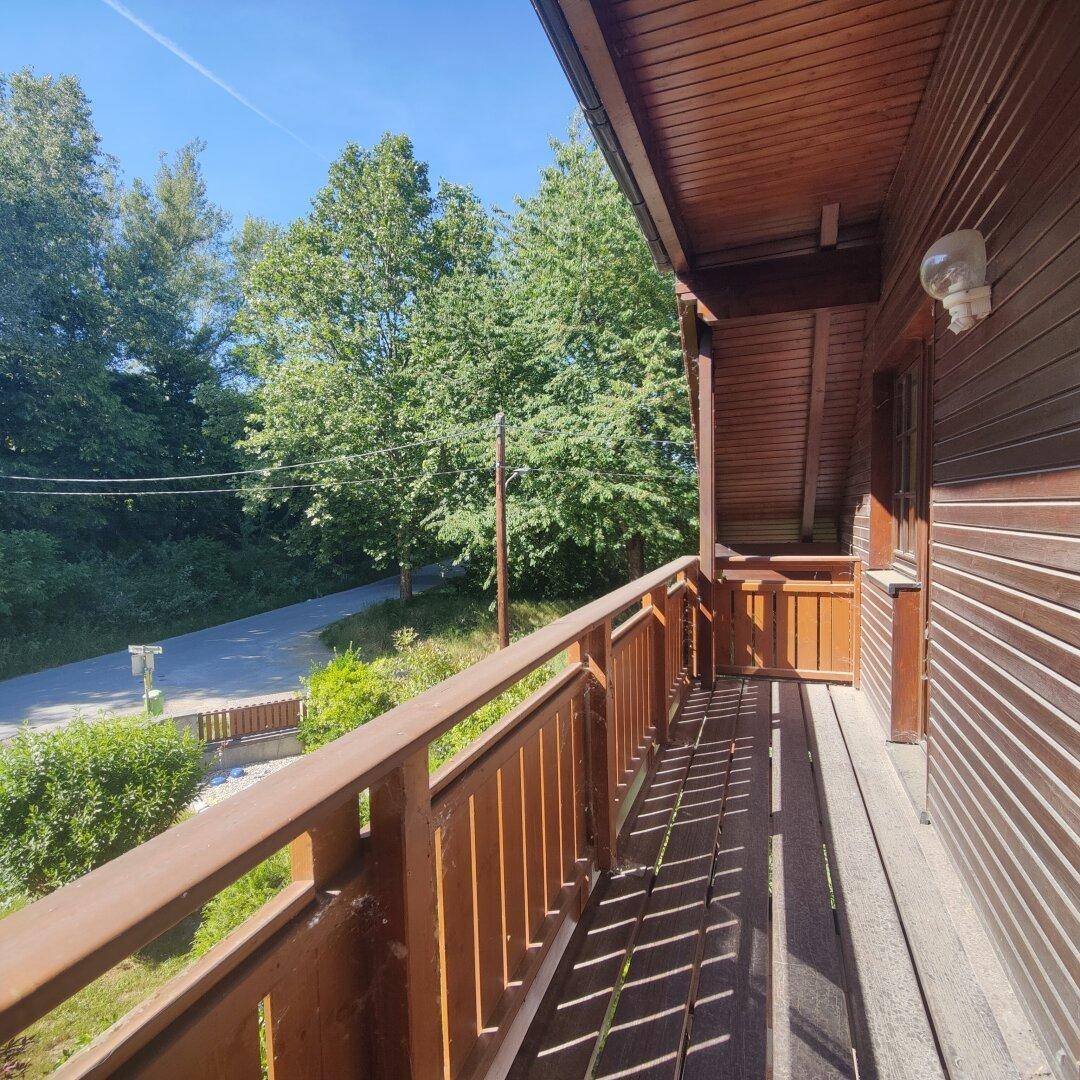 Balkon mit Holzgeländer und Blick auf Bäume und die umliegende Natur.