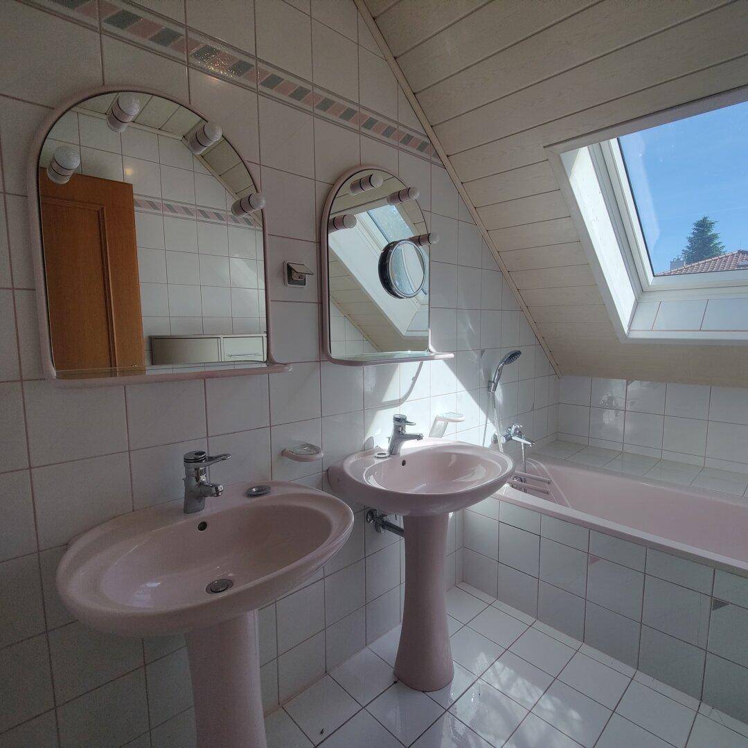 Badezimmer im Dachgeschoss mit zwei Waschbecken, Badewanne, weißen Fliesen und Dachfenster.