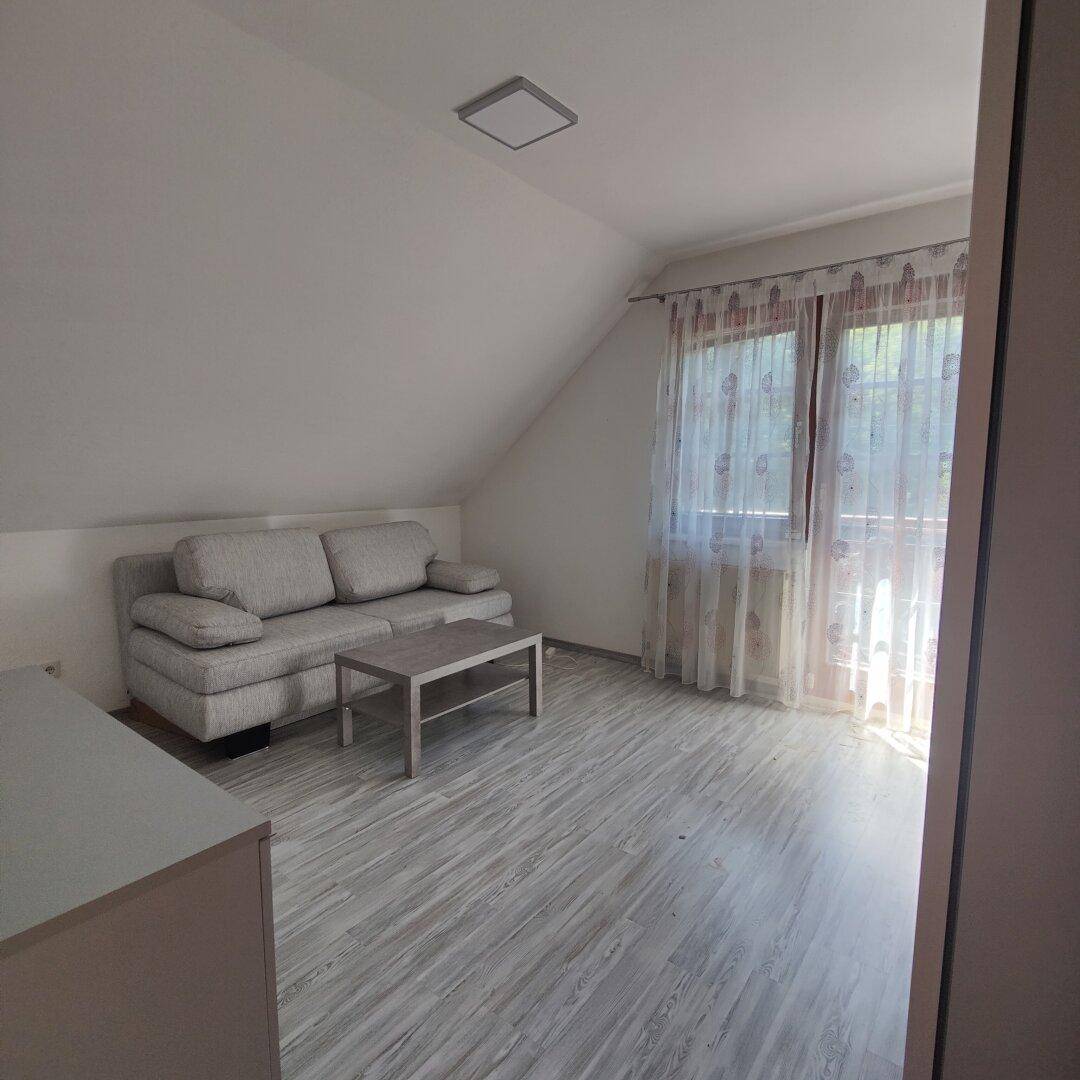 Gemütliches Wohnzimmer im Dachgeschoss mit Schrägdecke, Sofa und modernem Laminatboden.