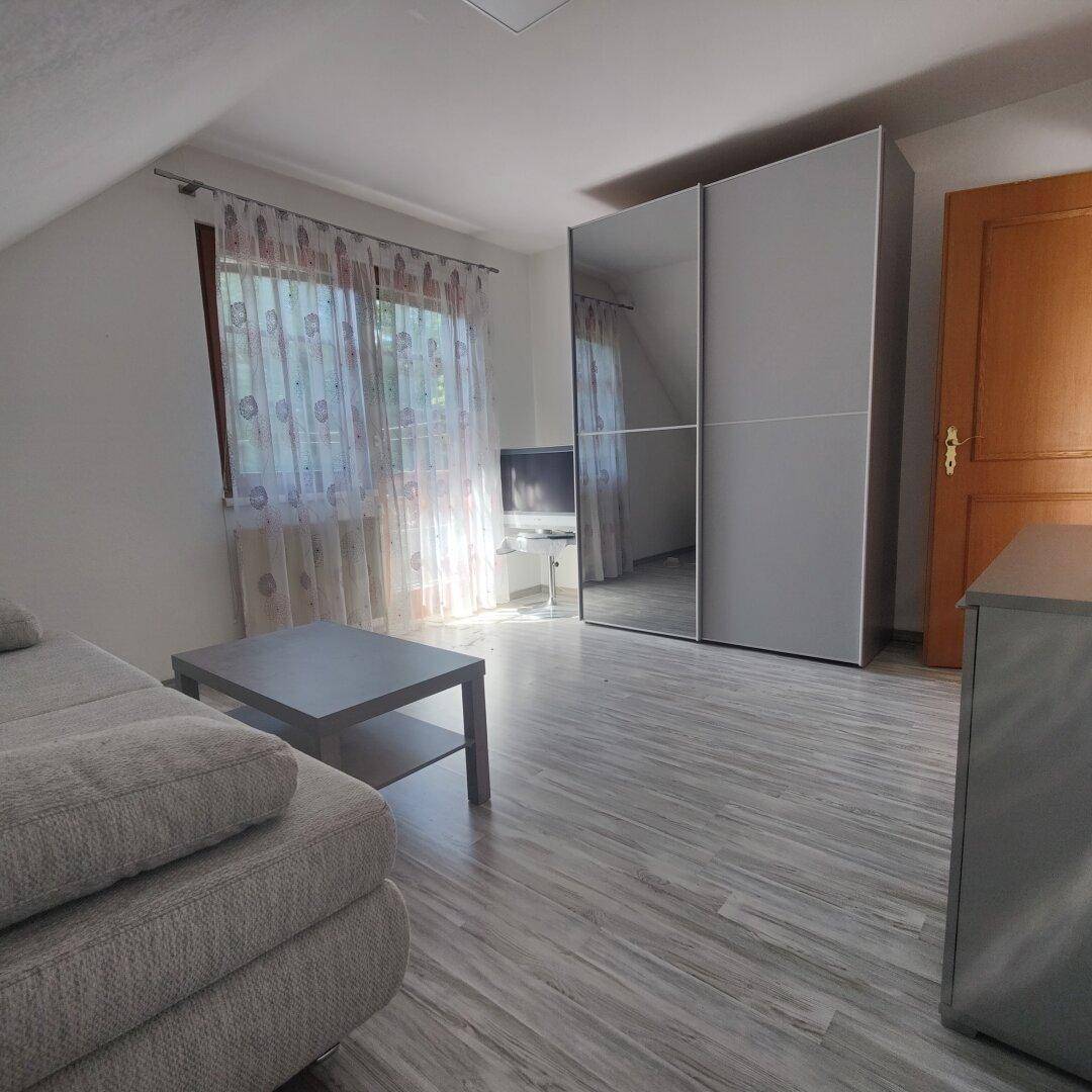 Wohnbereich im Dachgeschoss mit Schiebetürenschrank, Sofa und hellem Laminatboden.