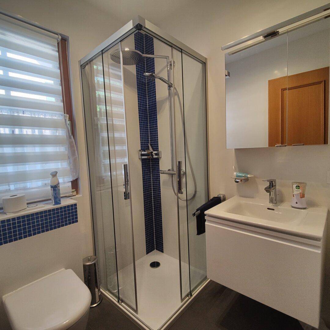 Modernes Badezimmer mit Eckdusche, WC, Einzelwaschbecken und Fenster.