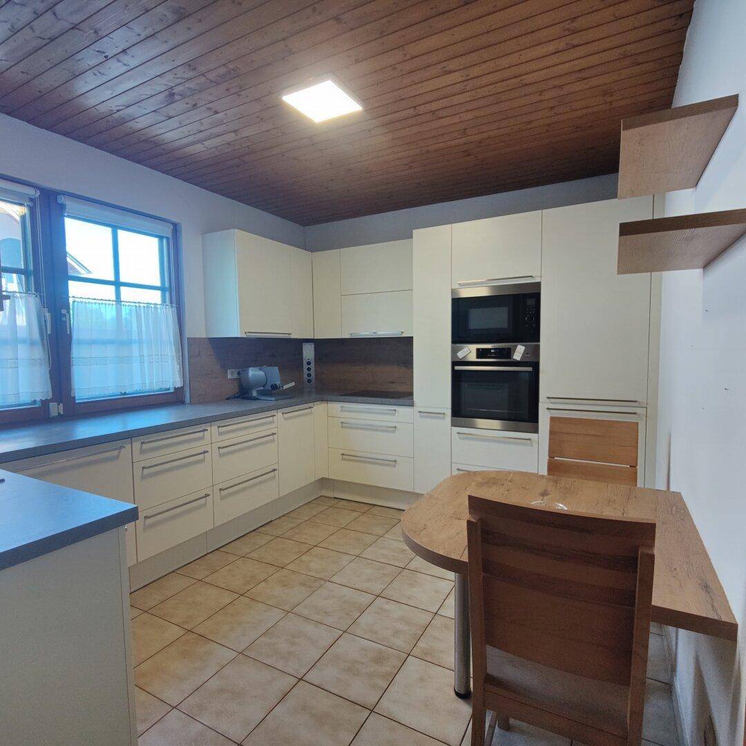 Moderne Küche mit weißen Schränken, Einbaugeräten, Essbereich und Holzdecke.