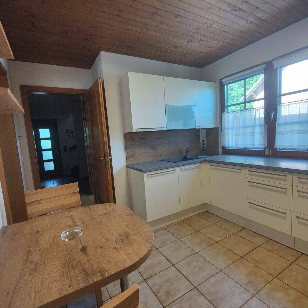 Helle Küche mit Spülbereich, Fenster und Zugang zum Flur, ausgestattet mit Holzdecke.