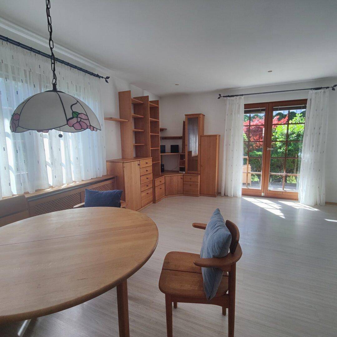 Heller Wohn-Essbereich mit Laminatboden, Holzmöbeln und Zugang zum Garten durch große Fenster.