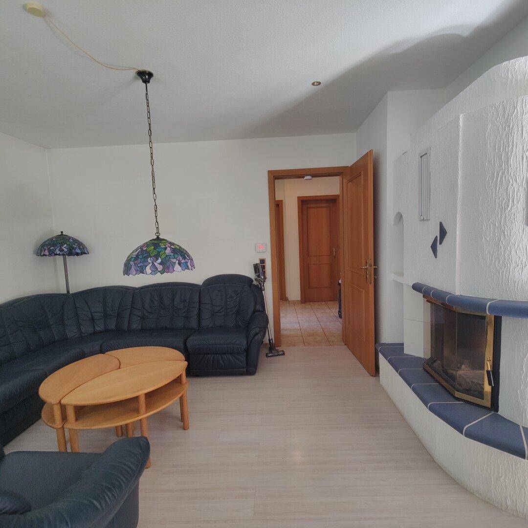 Wohnzimmer mit traditionellem Kachelofen, Ledersofa und Zugang zu weiteren Räumen.