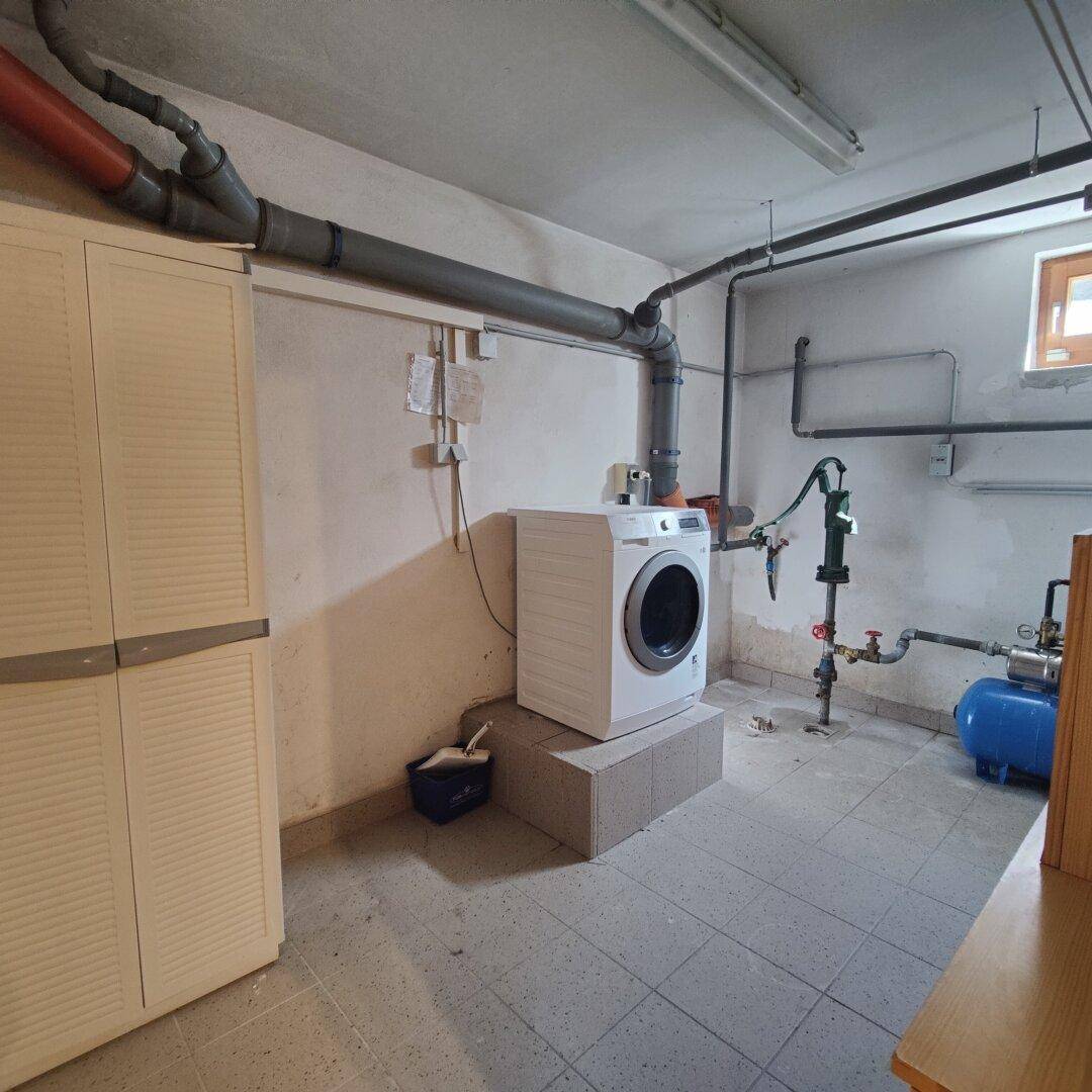 Hauswirtschaftsraum im Keller mit Waschmaschine, sichtbaren Leitungen und kleinem Fenster.