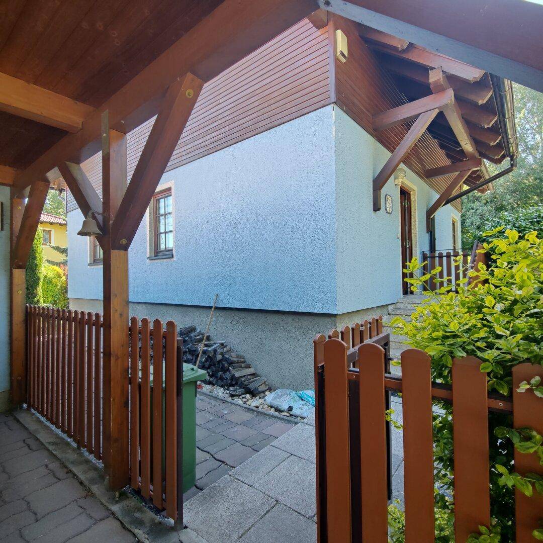 Seitenansicht des Hauses unter dem Carport, mit blauer Fassade und Holzelementen.