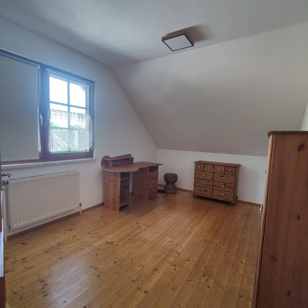 Helles Schlafzimmer im Dachgeschoss mit Holzdielenboden, Schreibtisch und Fenster.