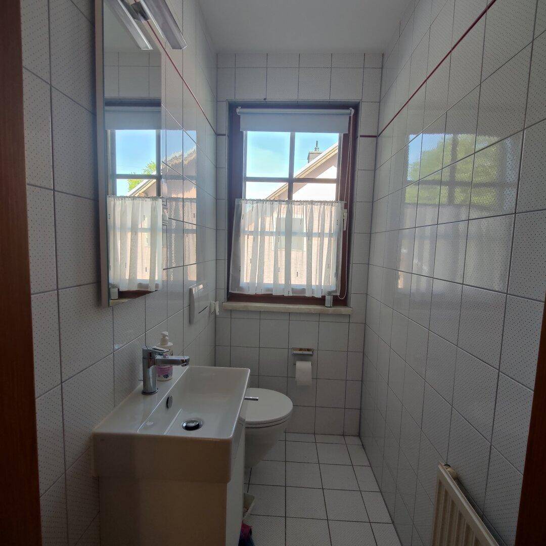 Kleines Gäste-WC mit Fenster, modernem Waschbecken und weißen Wand- und Bodenfliesen.