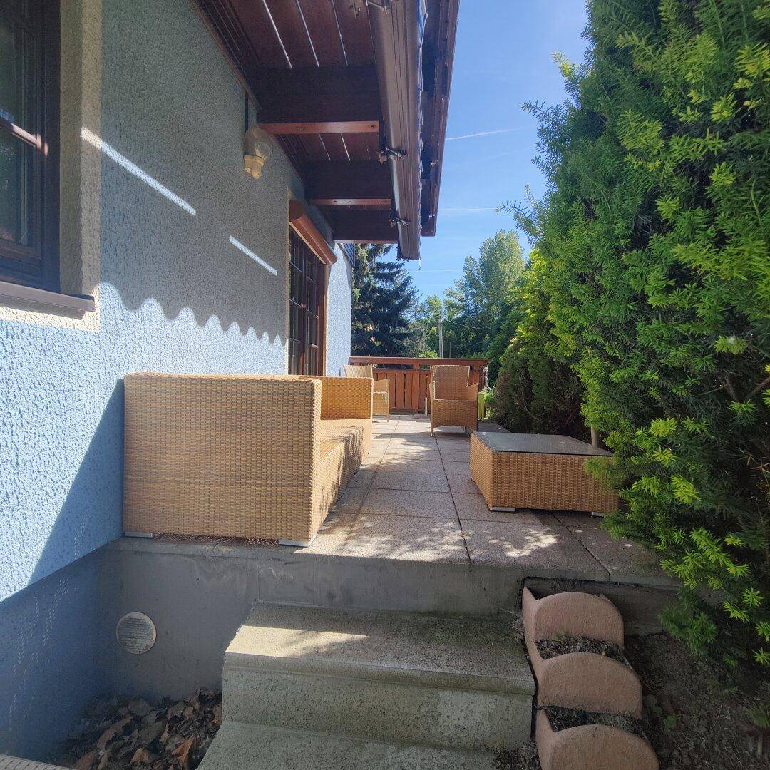 Terrassenbereich mit Stufen zum Garten, umgeben von üppigem Grün und viel Sonnenlicht.
