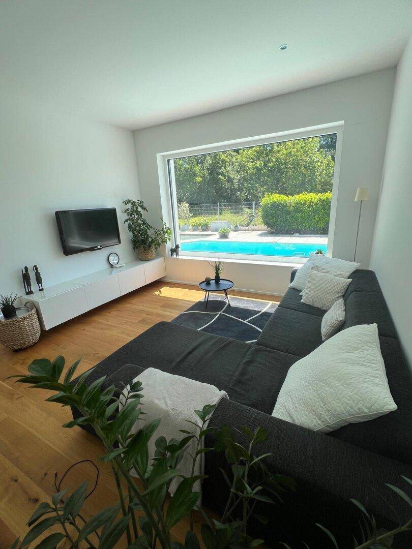 Gemütliches Wohnzimmer mit großem Sofa, Holzboden und direktem Blick auf den Poolbereich.