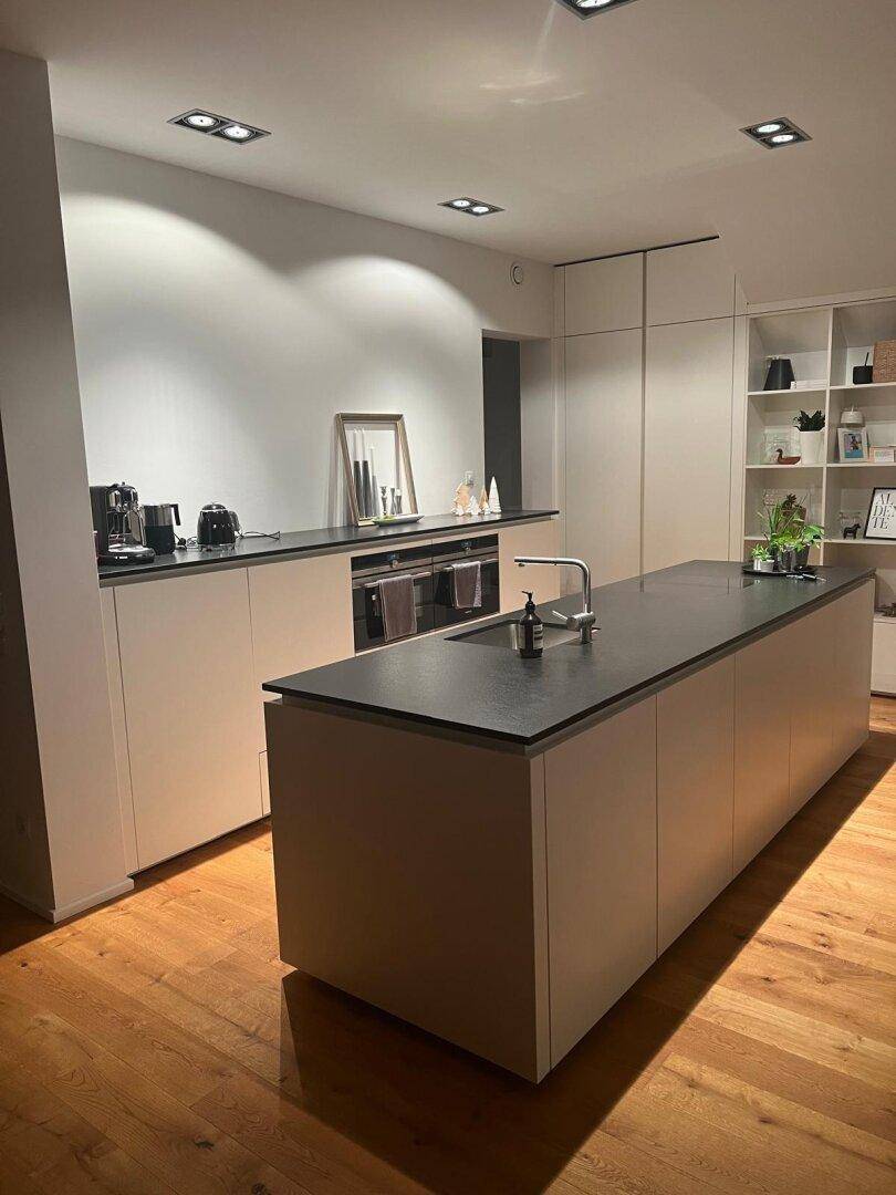 Elegante, moderne Küche mit großer Kochinsel, dunkler Arbeitsplatte und integrierten Geräten.