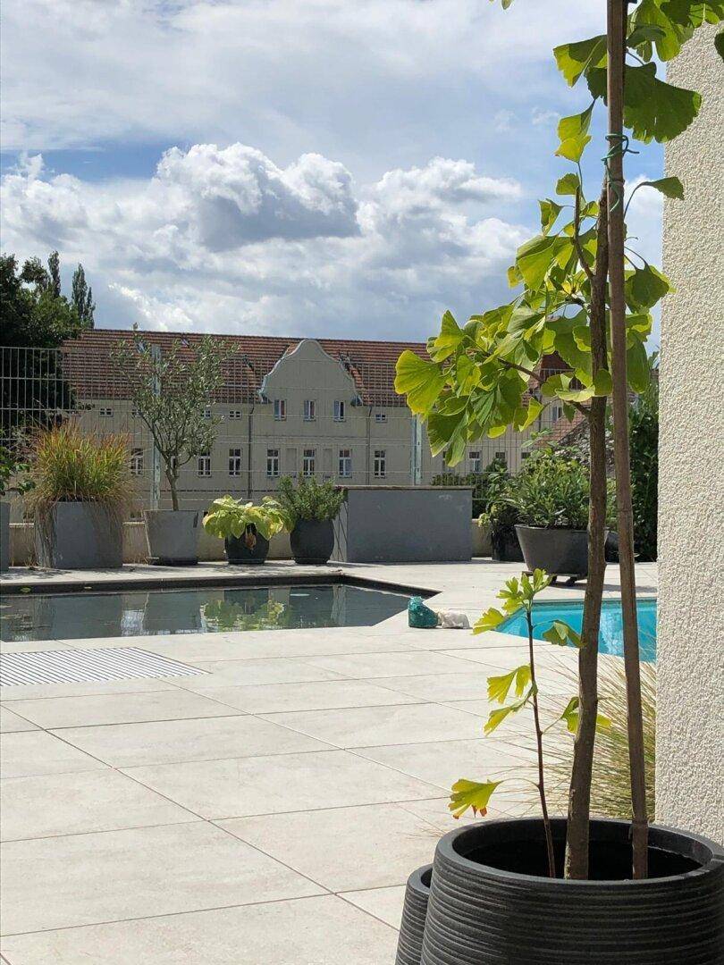 Außenbereich mit Pool und gepflasterter Fläche, im Hintergrund ist ein historisches Gebäude sichtbar.
