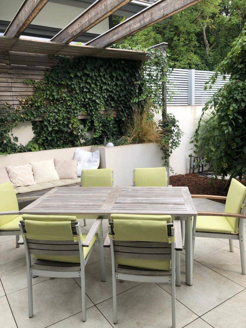 Gemütliche Außenterrasse mit Esstisch, Stühlen und einer begrünten Pergola.