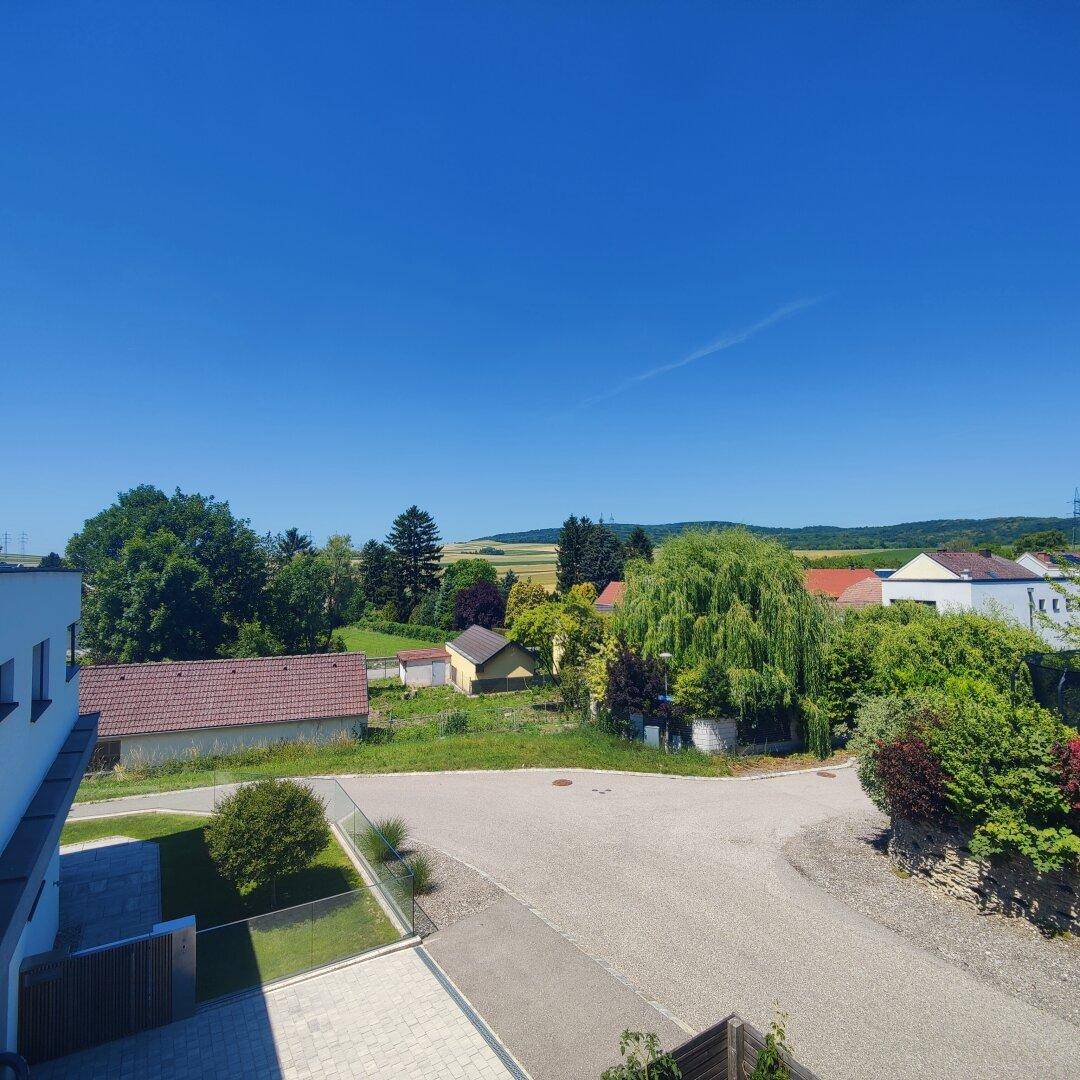 Weitläufiger Blick über die ländliche Umgebung mit Feldern und Bäumen unter blauem Himmel.