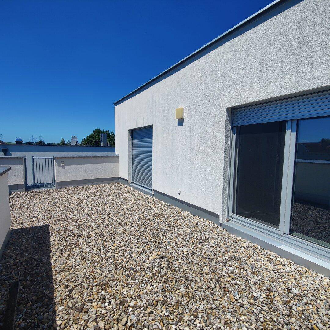 Geräumige Dachterrasse mit Kiesbelag und moderner Gebäudefassade im Hintergrund.