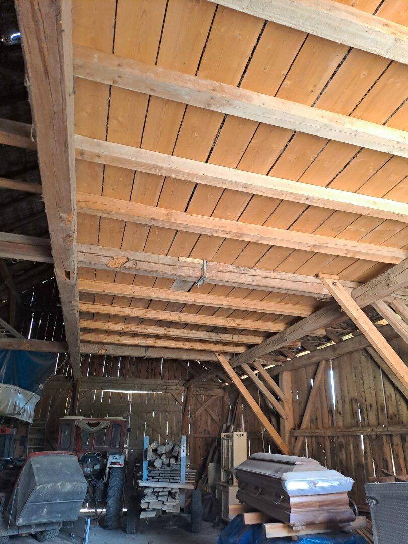 Innenansicht einer Scheune mit sichtbaren Holzbalken und einer Holzdecke.