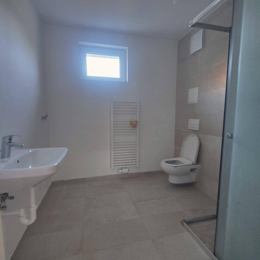 Modernes Badezimmer mit Dusche, wandhängendem WC, Waschbecken und beheiztem Handtuchhalter.