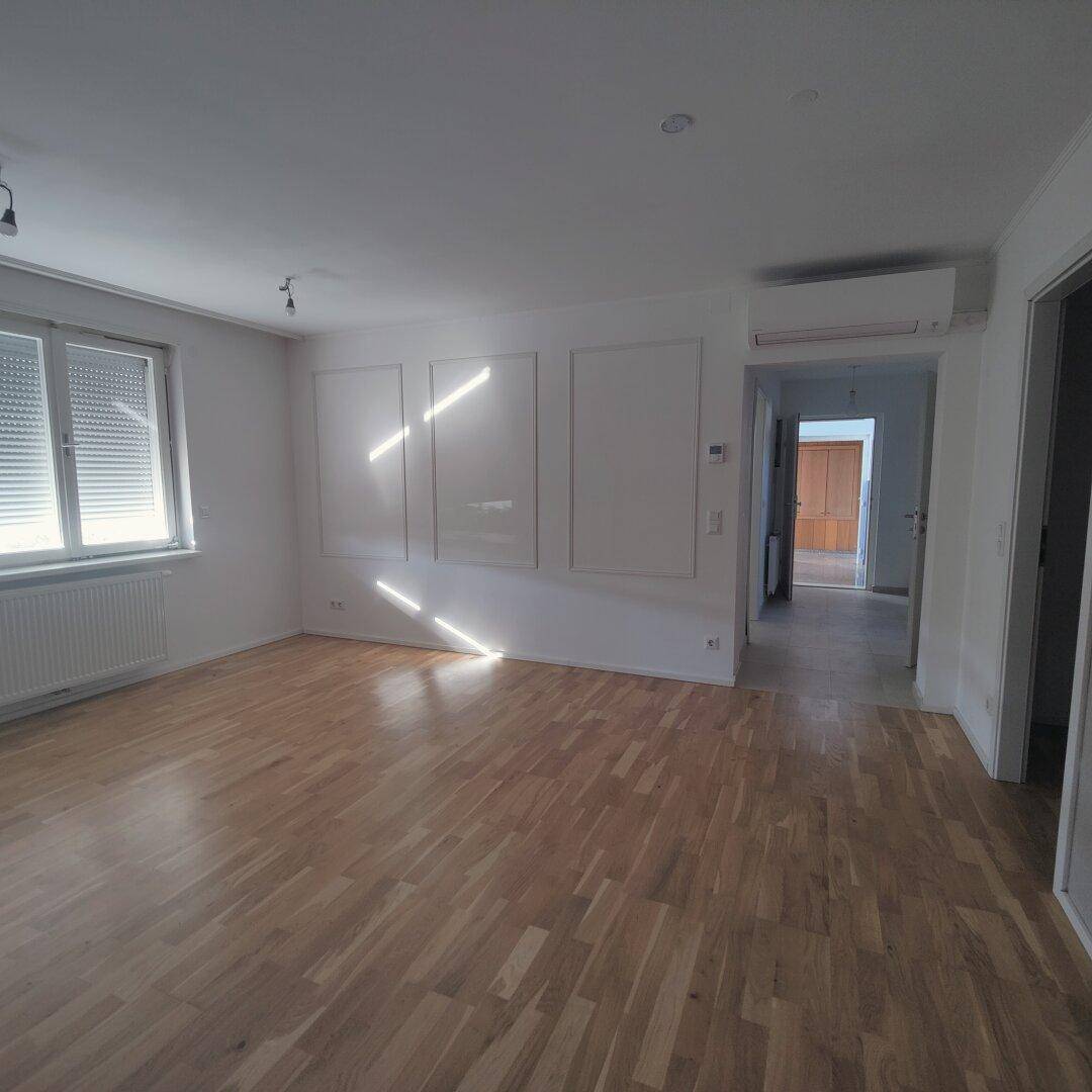 Lichtdurchfluteter Wohnraum mit Holzparkettboden, Klimaanlage und Fenster mit Rollladen.