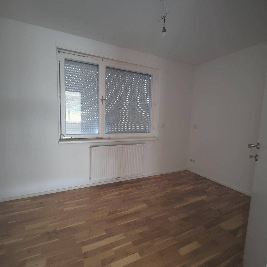 Gemütliches Schlafzimmer mit Holzparkettboden, Fenster mit Rollladen und ausreichend Tageslicht.