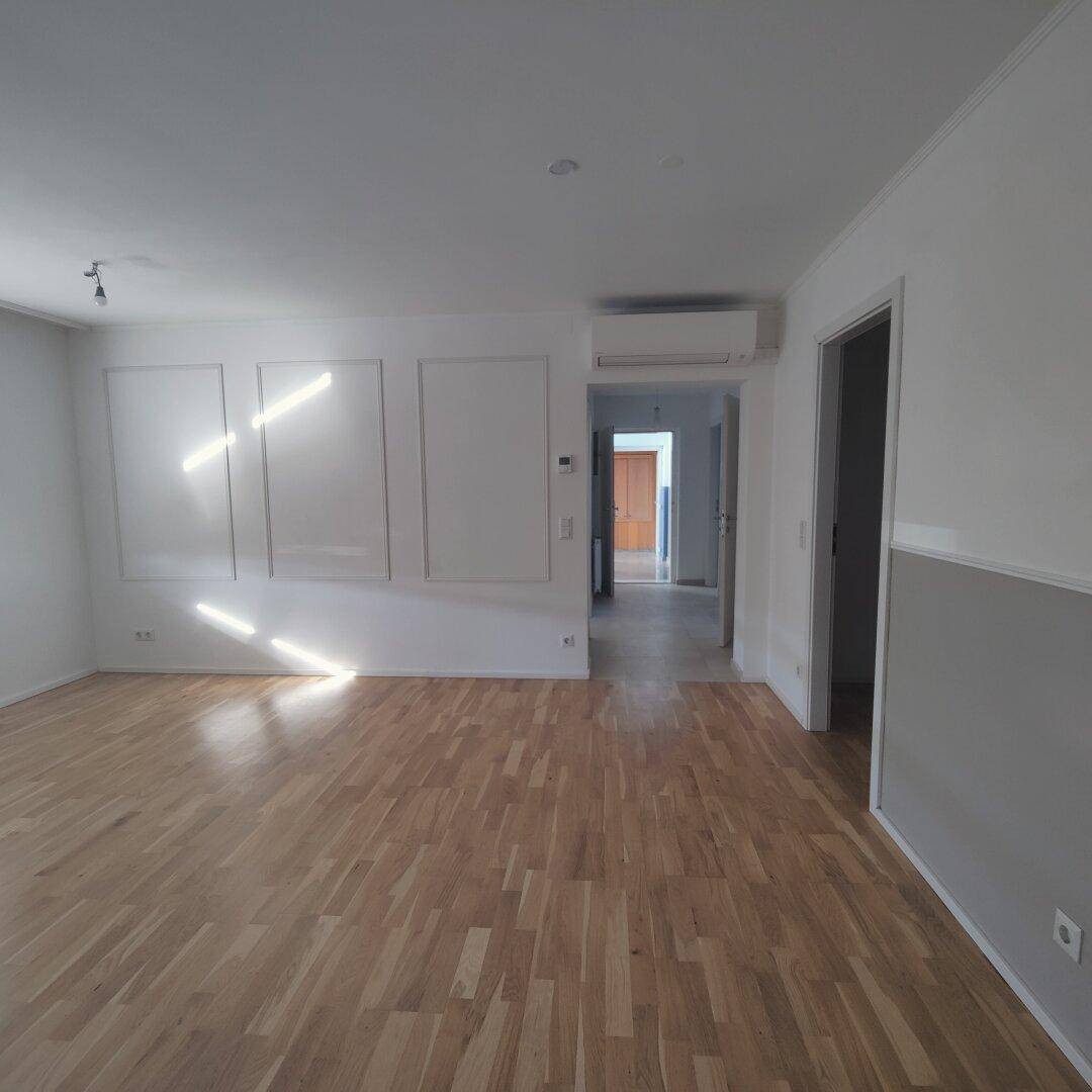 Geräumiger Wohnbereich mit Holzparkettboden, Klimaanlage und Zugang zu weiteren Zimmern.