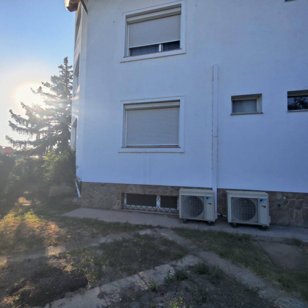 Seitenansicht des Hauses mit Klimaanlagen-Außengeräten und Fenstern mit Rollläden.