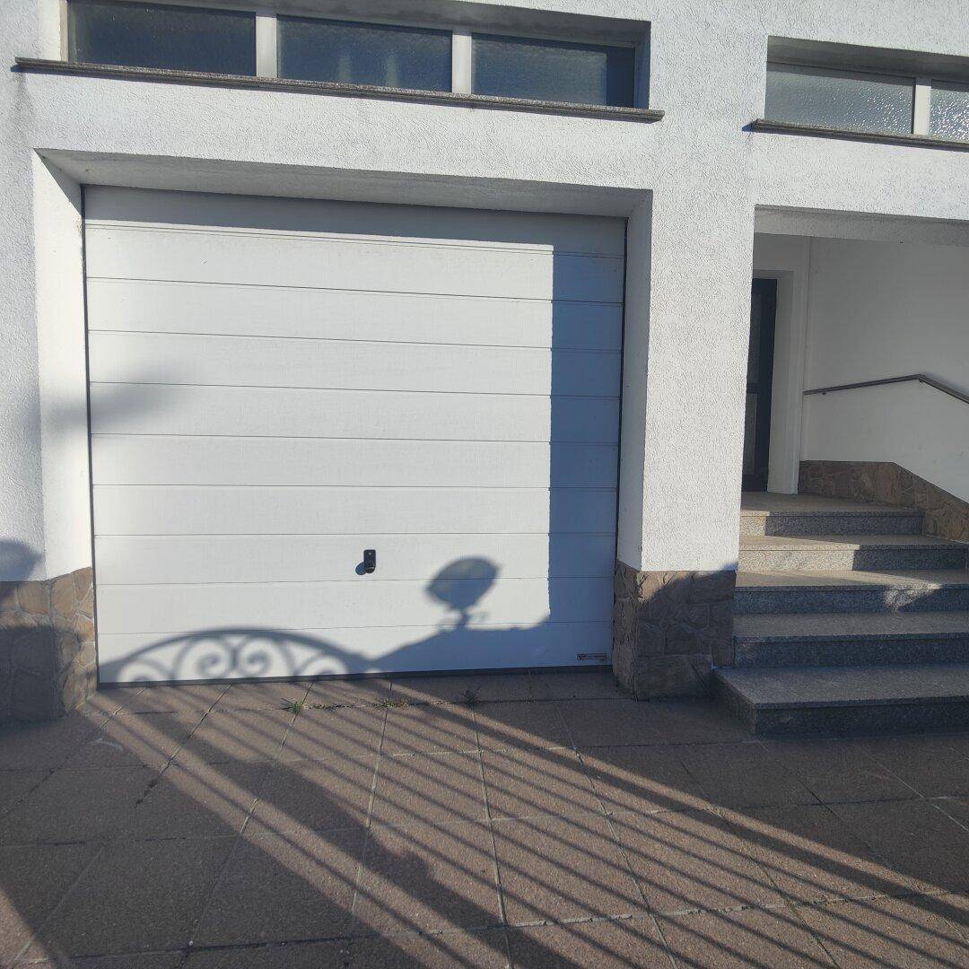 Weiße Garagentür mit horizontalen Lamellen und gepflastertem Vorplatz am Haus.