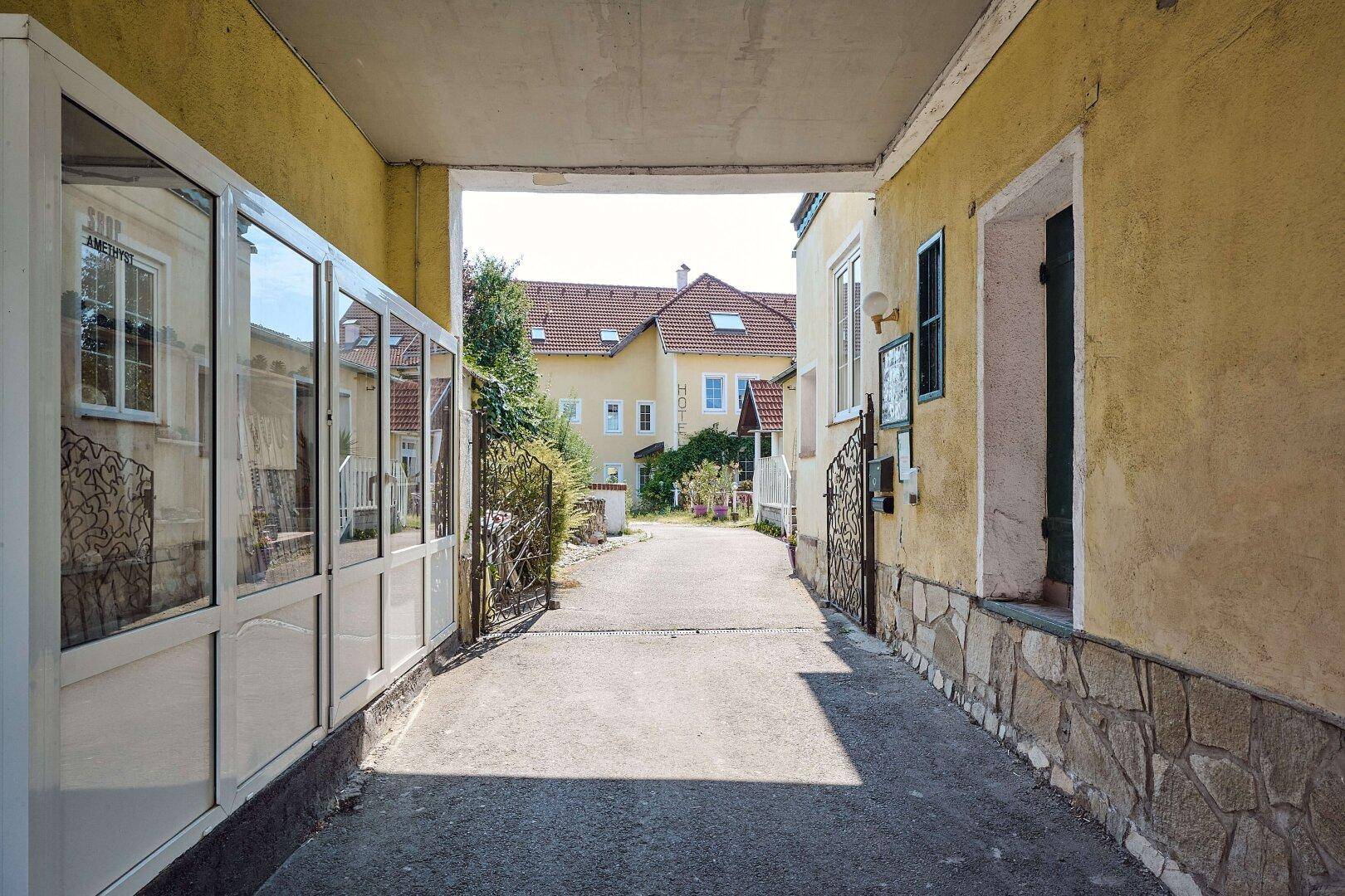 Ein schmaler Durchgang führt zu einem Innenhof, umgeben von Gebäuden mit gelben Fassaden.