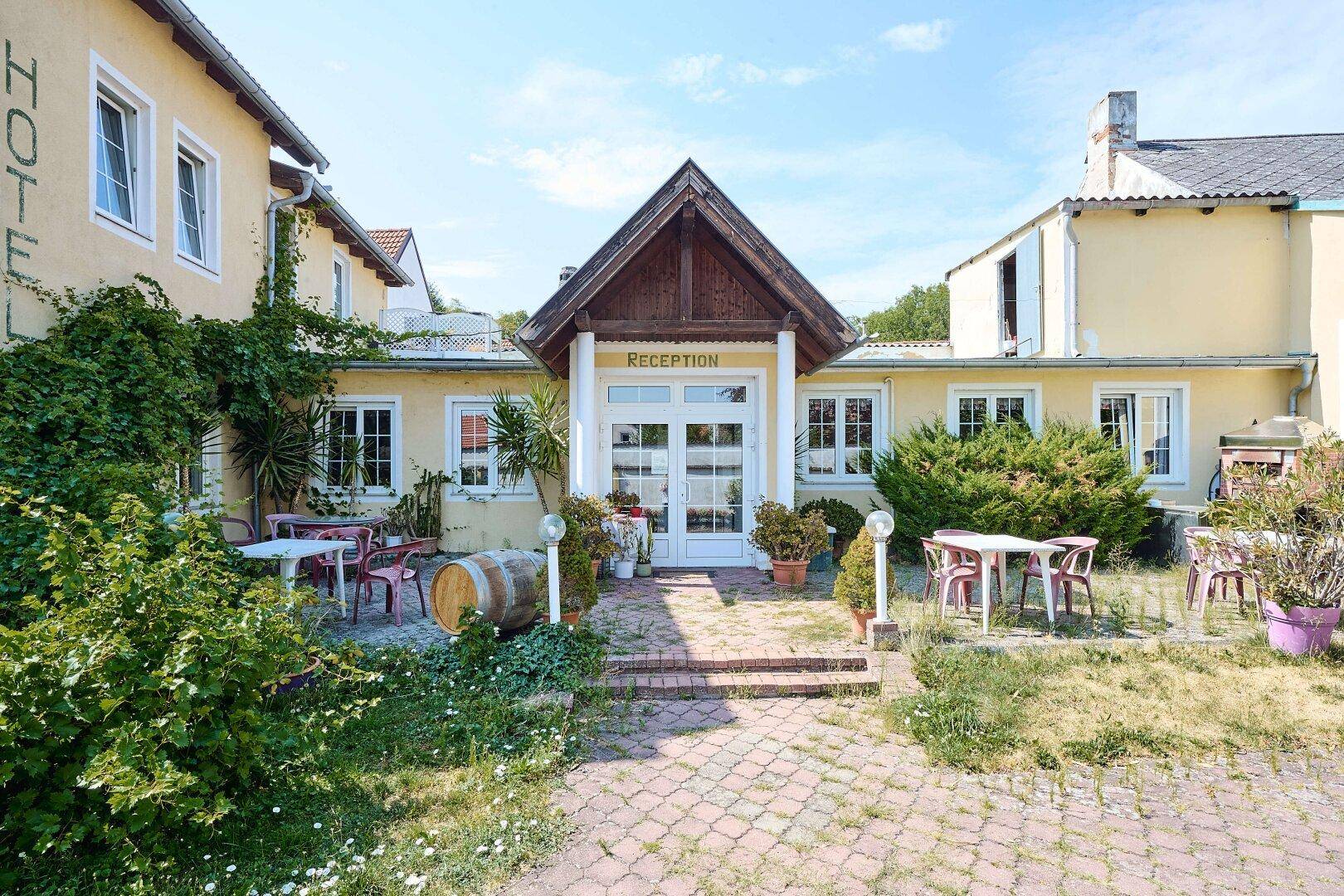 Der Hoteleingang mit "Reception"-Schild, umgeben von einer Terrasse mit Sitzgelegenheiten und Pflanzen.