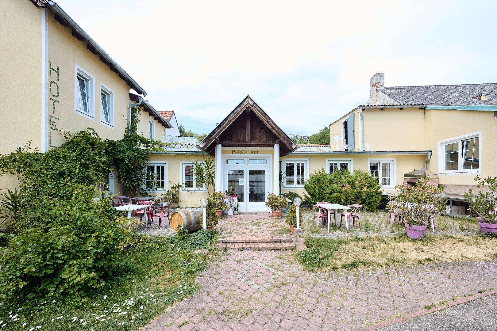 Der Hoteleingang mit "Reception"-Schild, umgeben von einer Terrasse mit Sitzgelegenheiten und Pflanzen.