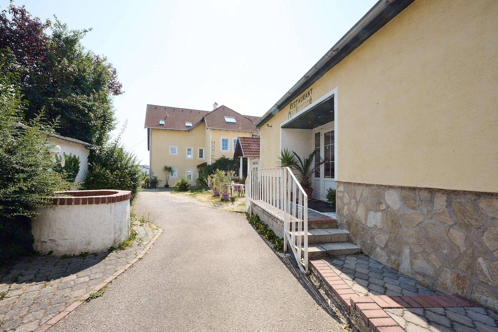 Ein gepflasterter Weg führt zum Hotel, rechts befindet sich der Eingang zum Restaurant "Mediterrane".