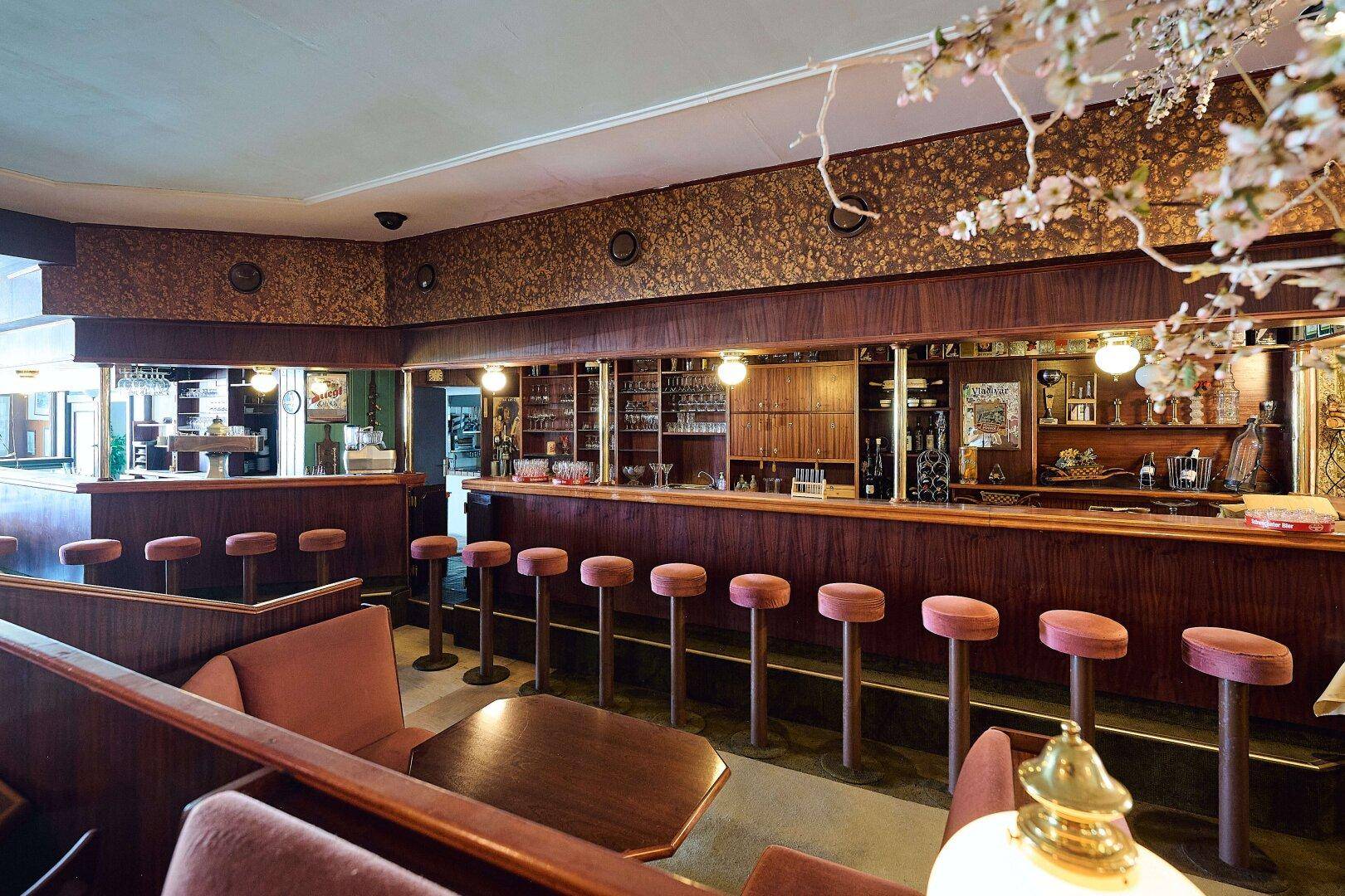 Detailansicht der Bar mit Holztheke, Hockern und Regalen voller Gläser und Flaschen.