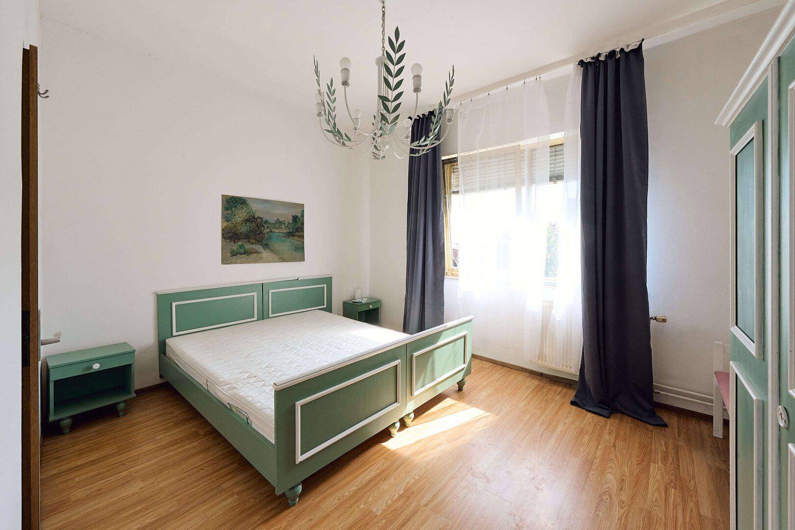 Helles Schlafzimmer mit grün gestrichenem Bettrahmen, passenden Nachttischen und Holzboden.